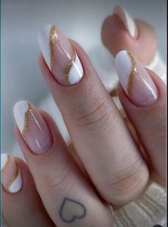 a woman's hand with white and gold manies on her nails, holding a heart