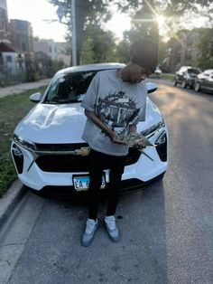 a young man sitting on the hood of a white car reading a book in front of him