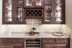 a kitchen with wooden cabinets and marble counter tops, wine glasses on the cabinet doors