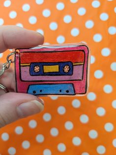 a hand holding a small keychain with a colorful cassette design on the front