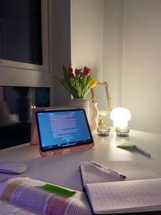 an open laptop computer sitting on top of a desk next to a lamp and notebook