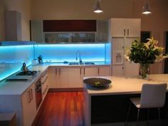 a modern kitchen with white cabinets and blue lights on the back splash, along with a center island