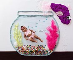 a baby in a pink swimsuit laying on top of a fish bowl filled with candy