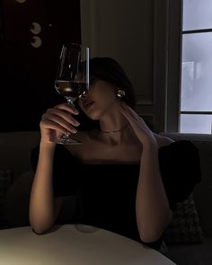 a woman sitting at a table with a glass of wine in front of her face