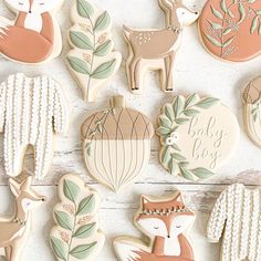 baby shower cookies are arranged on a white wooden surface with leaves and deers in the background