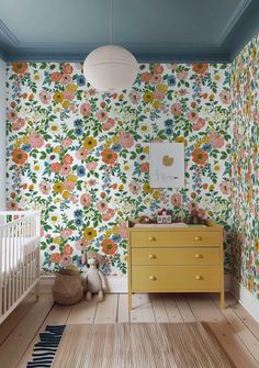 a baby's room with floral wallpaper and yellow dresser in the foreground