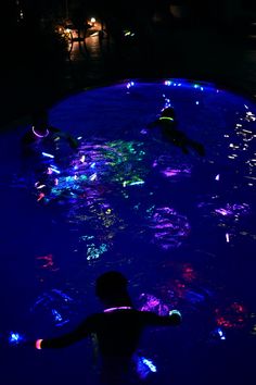 people are swimming in the water at night with lights on them and their arms spread out