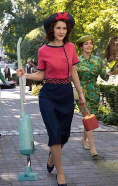 two women are walking down the street with luggage and hats on their heads, one is holding an owl