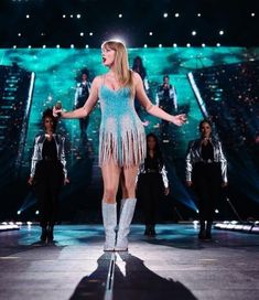 a woman in a fringe dress on stage with other people behind her and one person wearing boots