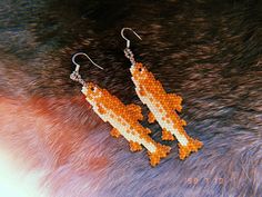 an orange and white beaded pair of earrings sitting on top of a furry surface