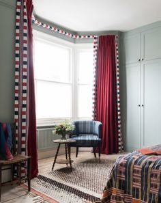 a bedroom with red curtains and a blue chair in front of the window, next to a rug on the floor