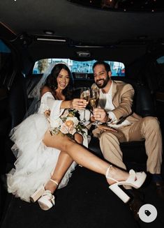 a bride and groom sitting in the back of a limo holding champagne flutes, toasting