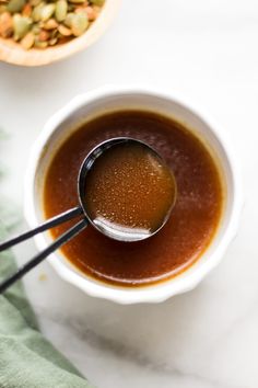 a spoon in a bowl filled with liquid and nuts next to a cup of soup