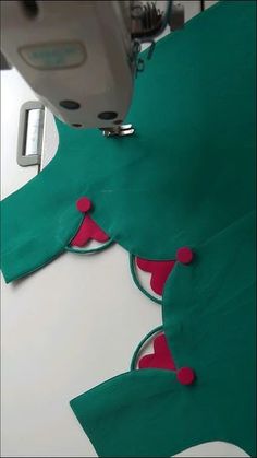 the sewing machine is working on the green fabric with red circles and pink dots around it