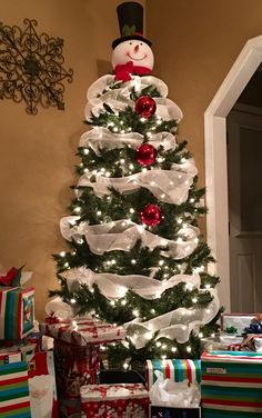 a christmas tree with presents under it and a snowman decoration on the top,