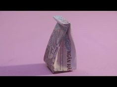 an origami money bag sitting on top of a pink surface with purple background