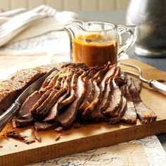 a cutting board topped with sliced meat next to a jar of sauce