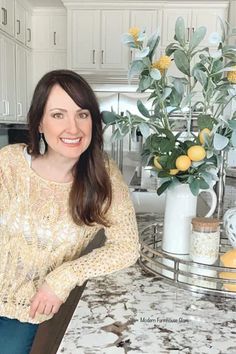 a woman sitting at a kitchen counter in front of a vase with lemons on it