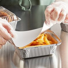 a person in white gloves is taking food out of a tin foil container