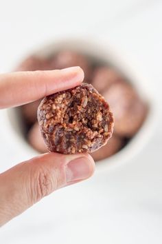 a hand holding a piece of food in front of a white bowl filled with nuts