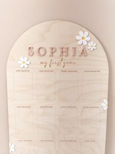 a wooden calendar with white flowers on the front and pink lettering that says sophia my first year