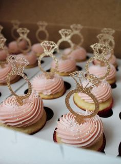 cupcakes with pink frosting and gold decorations are arranged on a white tray