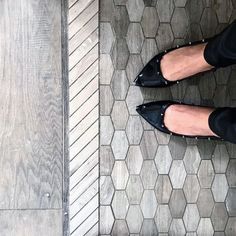 a woman's feet in black shoes standing on a tile floor with hexagonal tiles