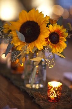 there is a vase with sunflowers and a candle in it on the table