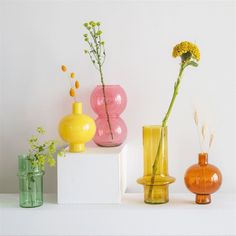 three different colored vases sitting on top of a white shelf next to each other