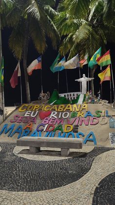 there is a bench with graffiti on it in front of some palm trees and flags