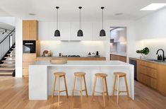 an open kitchen with three stools next to the counter and stairs leading up to the second floor