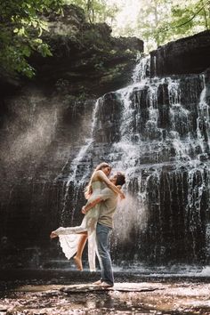 a man and woman standing in front of a waterfall with their arms around each other