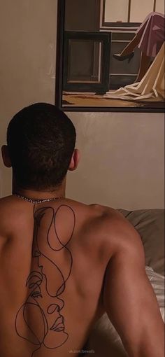 a man with a tattoo on his back sitting in front of a mirror looking at himself