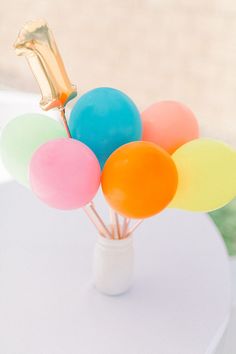 colorful balloons in a vase on top of a white table with a gold balloon centerpiece