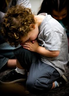 a little boy sitting on the ground with his head in his hands