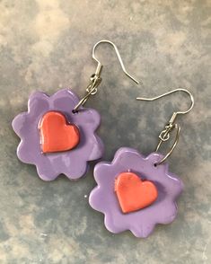 two purple and orange flower shaped earrings with hearts on them, sitting on a gray surface