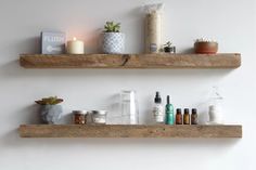 two wooden shelves with candles, bottles and other items on them in a white room