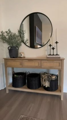 a wooden table with two baskets and a round mirror on the wall above it,