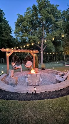 a fire pit in the middle of a yard with lights strung around it and two chairs