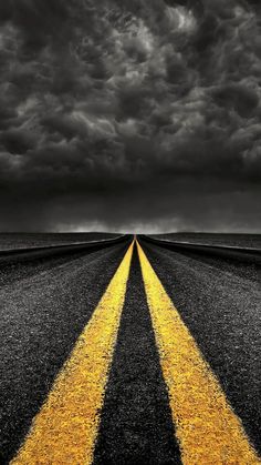 an empty road with two yellow arrows painted on it under a dark sky filled with clouds