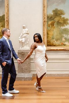 a man and woman holding hands in front of paintings