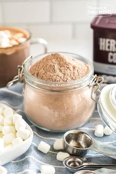 hot chocolate mix in a glass jar with marshmallows on the table next to it