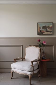 a white chair sitting in front of a painting on the wall next to a table