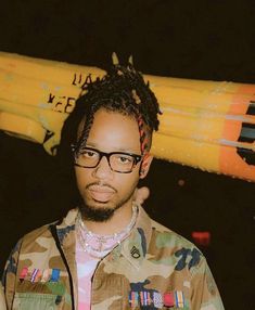 a man wearing glasses standing in front of a yellow surfboard on top of his head