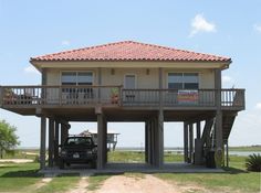 a car is parked in front of a two story house on stilts overlooking the ocean