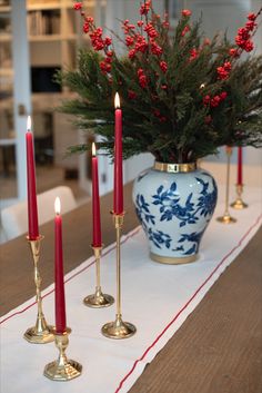 three candles are sitting on a table with red berries in a blue and white vase