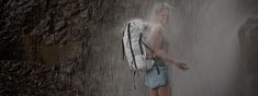 a man standing in front of a waterfall with a backpack on his back and water coming out of it