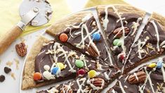 there is a chocolate pizza with nuts and candy toppings on the plate next to a spatula