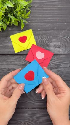 two hands are holding small pieces of paper with hearts on them, and one hand is holding an origami heart