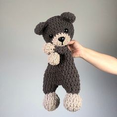 a hand holding a crocheted teddy bear in front of a gray background,